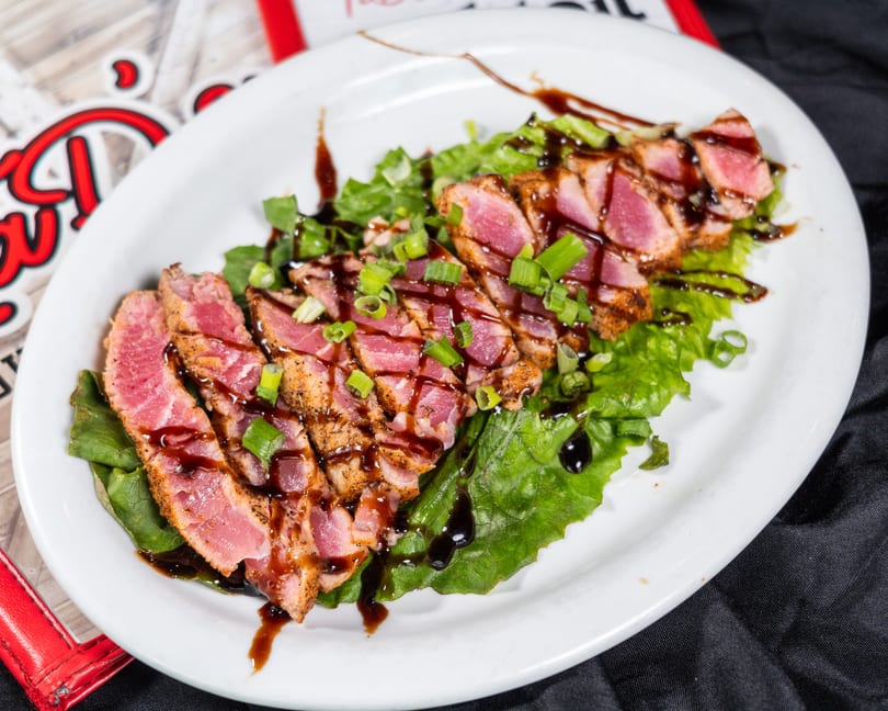 Seared tuna slices with green onions and balsamic glaze on a bed of lettuce.