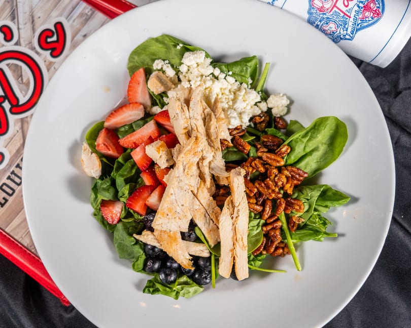A vibrant salad with spinach, grilled chicken, strawberries, blueberries, pecans, and feta cheese.