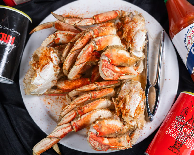 A plate of seasoned crab legs with a crab cracker, hot sauce, and seasoning containers.