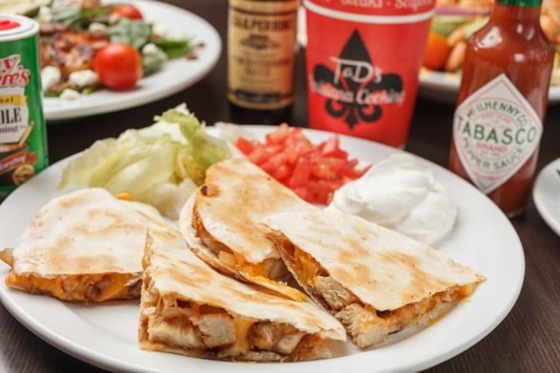 Chicken quesadillas with lettuce, diced tomatoes, and sour cream, alongside Tabasco sauce and seasoning.